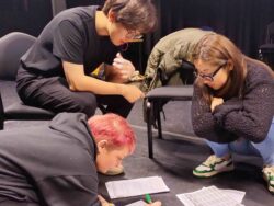 Three people sitting or kneeling on the floor writing poems on pieces of paper