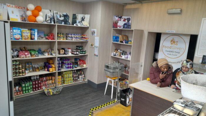 Food and other items in a community social food hub. Two women in conversation, one is talking on a mobile phone.