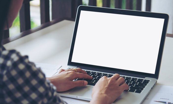 Image shows a person wearing a blue and white checked shirt, typing into a computer.