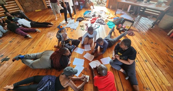 A group of young people lay on a wooden floor with sheets of coloured paper between them